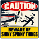 A novelty warning sign with a red 'CAUTION' header and a yellow bottom banner reading 'BEWARE OF SHINY SPINNY THINGS.' The center shows a retro airplane and a falling black stick figure on a cream background.
