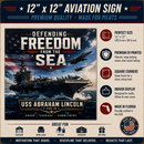 An aviation sign featuring a military-themed graphic with the text 'Defending Freedom from the Sea' and 'USS Abraham Lincoln CVN-76,' shown on a beige background with feature callouts and icons.
