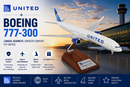 Model of a United Boeing 777-300 airplane on a wooden stand with sunset airport background.