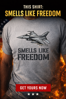 Gray t-shirt with fighter jet graphic and 'Smells Like Freedom' text, American flag in background